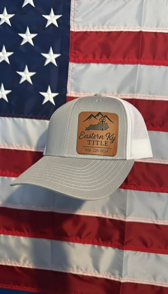 A light gray hat with &ldquo;Eastern Ky Title&rdquo; logo is displayed in front of a large American flag.