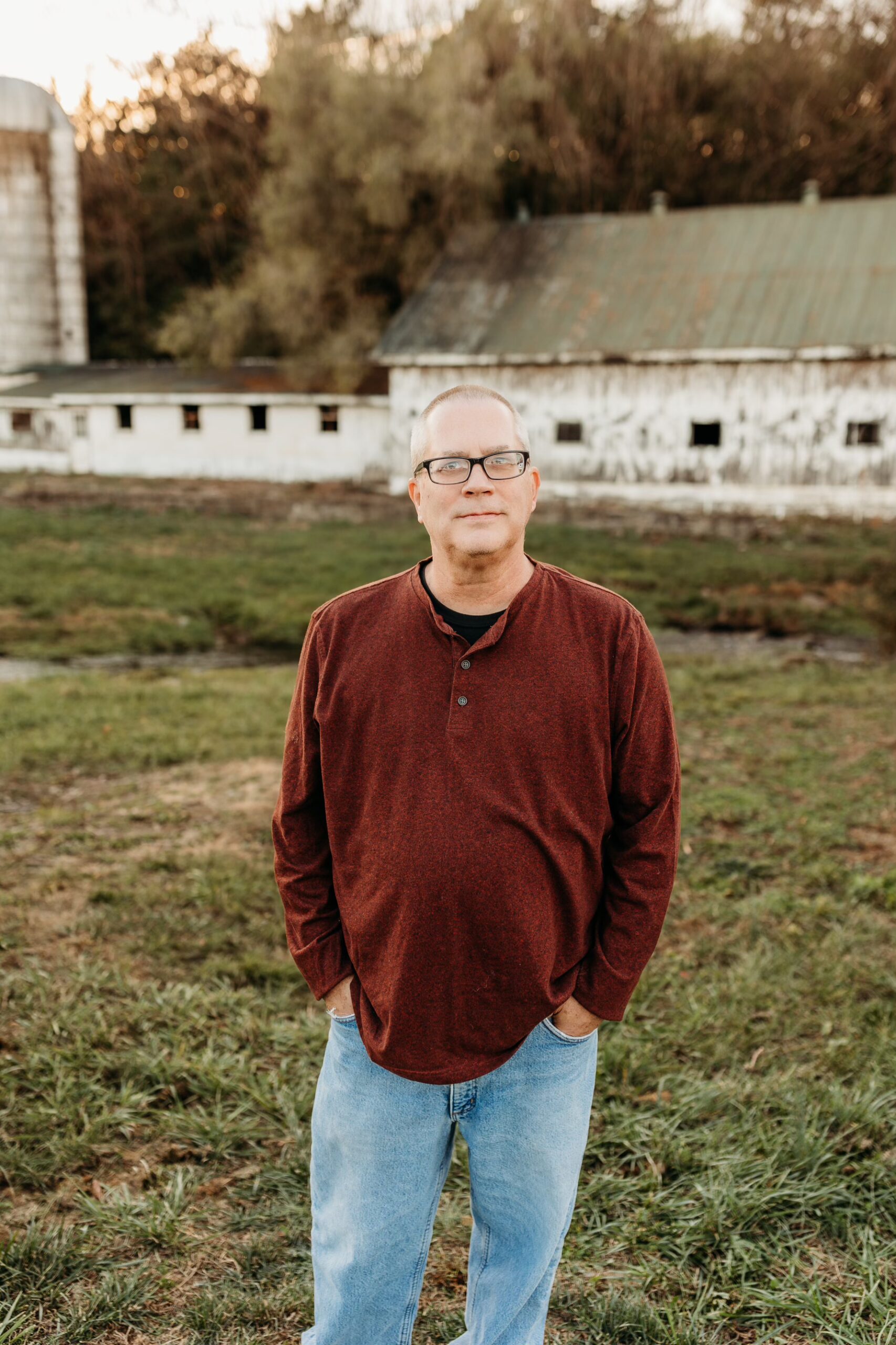 A man with a beard smiles while holding two young children, both smiling, standing outside in front of a house with flowers and a wreath on the door.